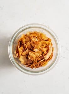 Glass jar of vegan coconut bacon sitting on a white surface.