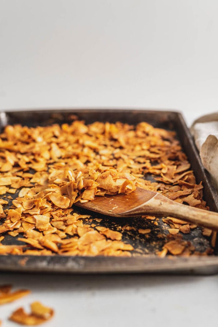 Coconut bacon on a baking try with a wooden spatula.