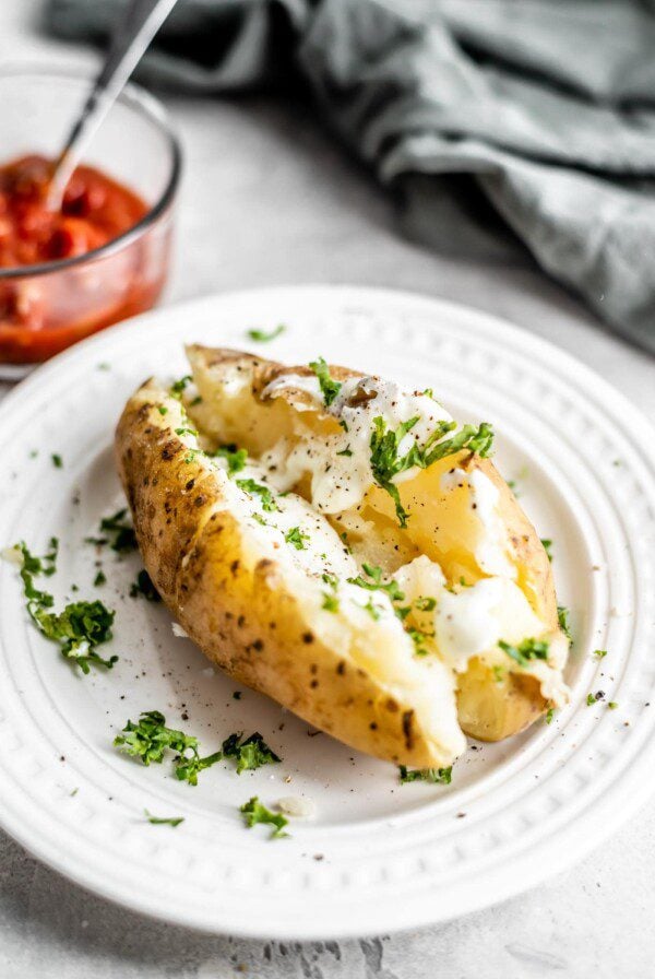 A baked potato topped with sour cream and parsley on a small white plate.