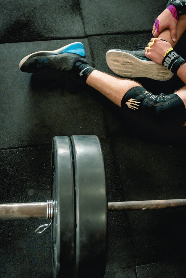 Person sitting on a gym floor beside a barbell with weight plates on it.