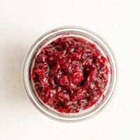 Overhead image of a glass far filled with homemade cranberry sauce sitting on a white surface.