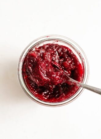 Overhead image of a glass far filled with homemade cranberry sauce sitting on a white surface.