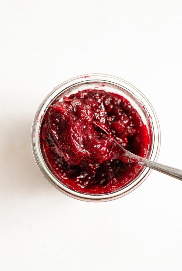 Overhead image of a glass far filled with homemade cranberry sauce sitting on a white surface.