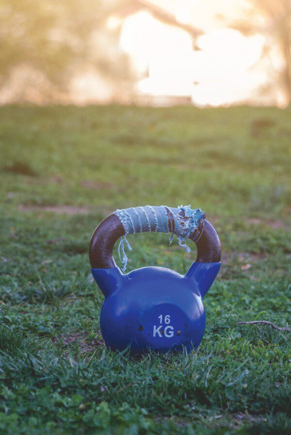 A blue kettlebell sitting in a grassy field.