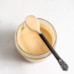 A spoon scooping miso tahini dressing out of a small glass jar.