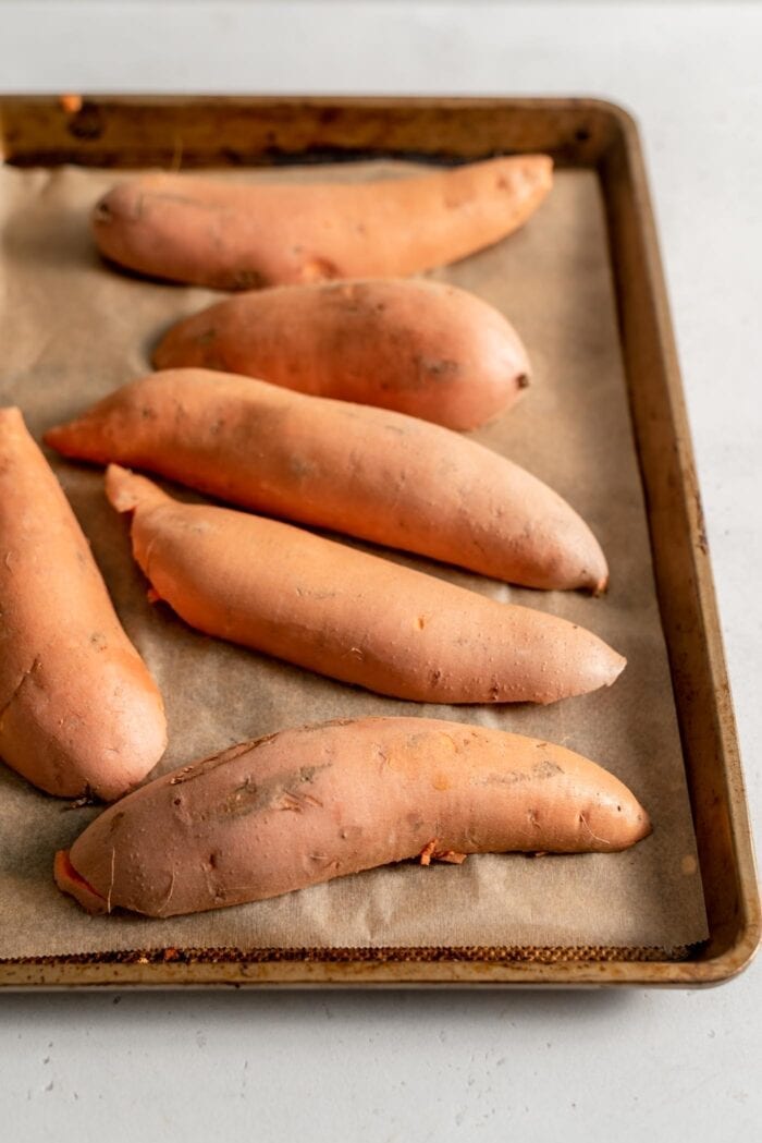 Sweet potatoes cut in half and placed face down on a baking tray lined with parchment paper.