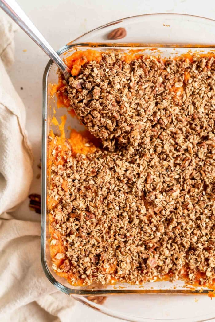 A spoon scooping sweet potato casserole out of a baking dish.