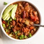 A bowl of vegan chili topped with avocado and green onion.