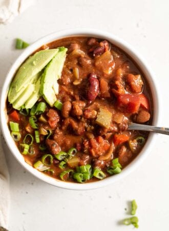 A bowl of vegan chili topped with avocado and green onion.