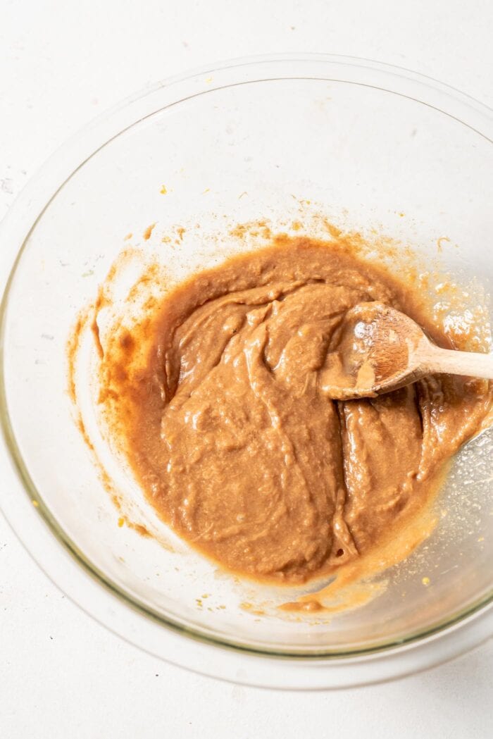 Maple syrup and almond butter mixed together in a glass mixing bowl.