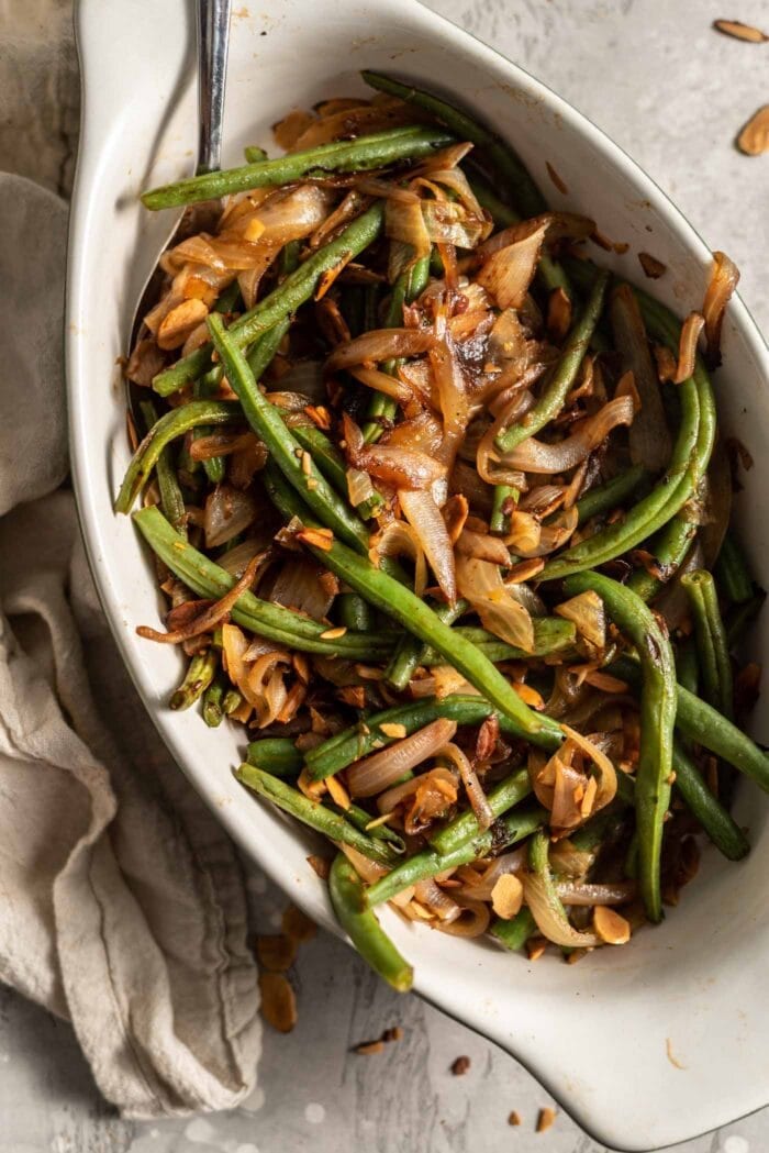 Sauteed green beans with onions, garlic and slivered almonds in a serving dish with a spoon.