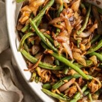 Sauteed green beans with onions, garlic and slivered almonds in a serving dish with a spoon.