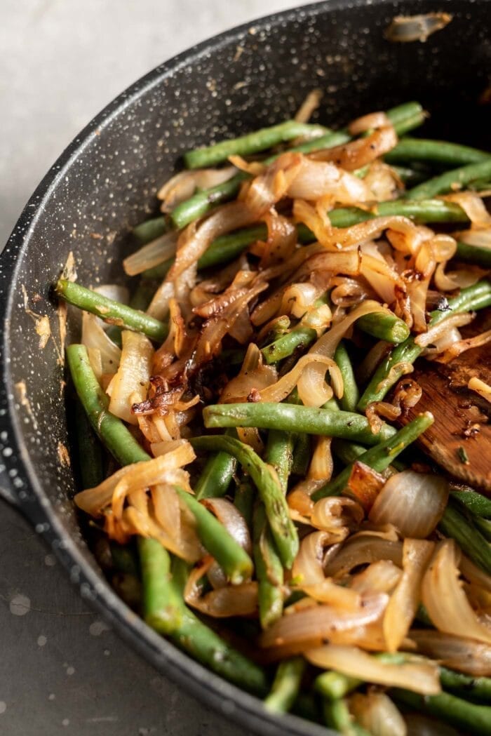 Sautéed green beans and onions in a black skillet.