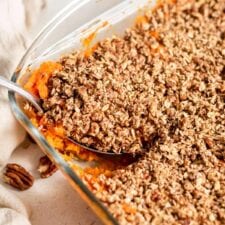 Scooping out a serving of sweet potato casserole out of a baking dish.