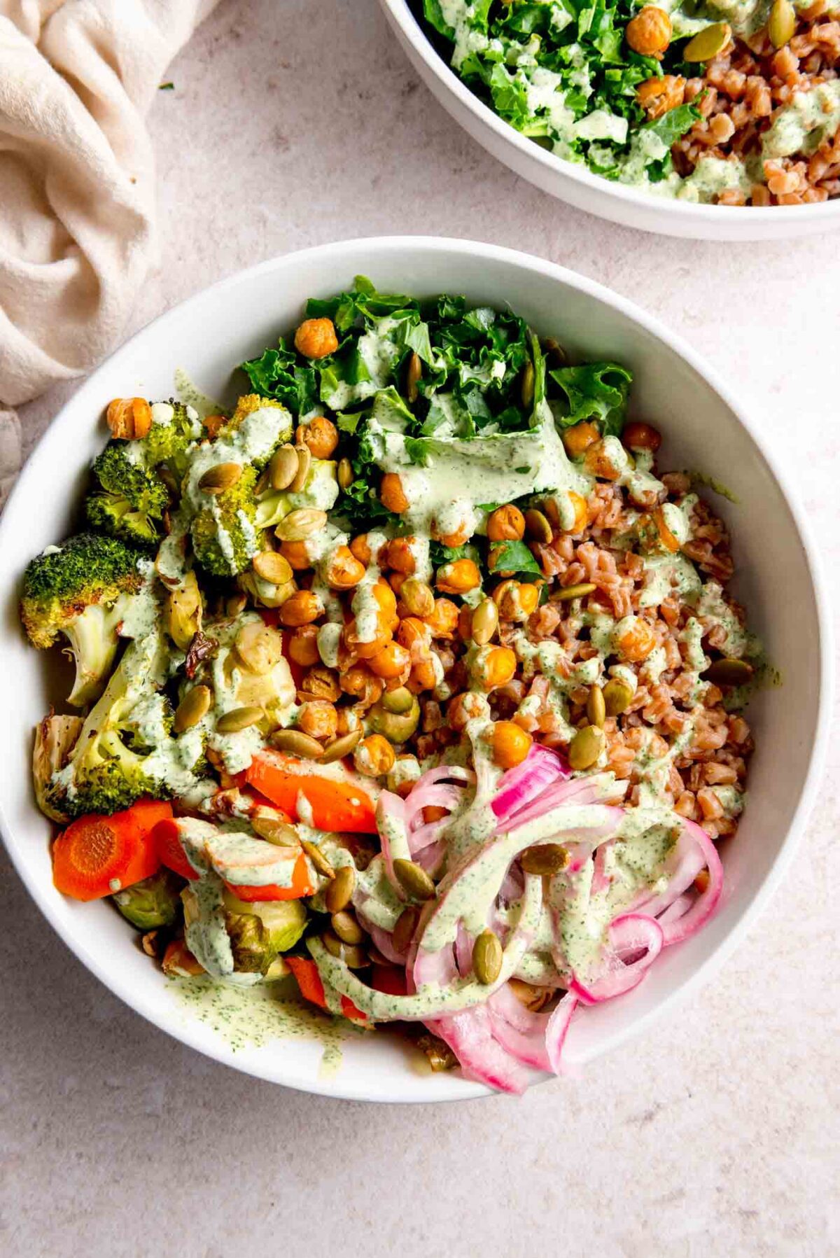 Bowl with farro, chickpeas, roasted vegetables, kale, pickled onion and a creamy sauce.