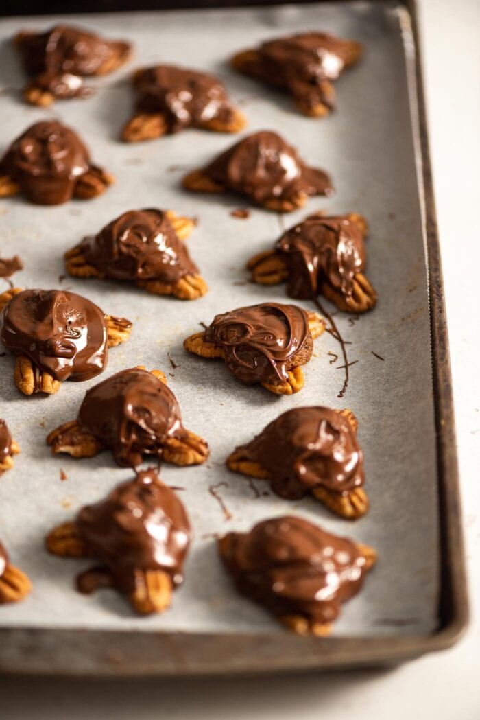 Dates and pecans covered in melted chocolate on a baking tray.