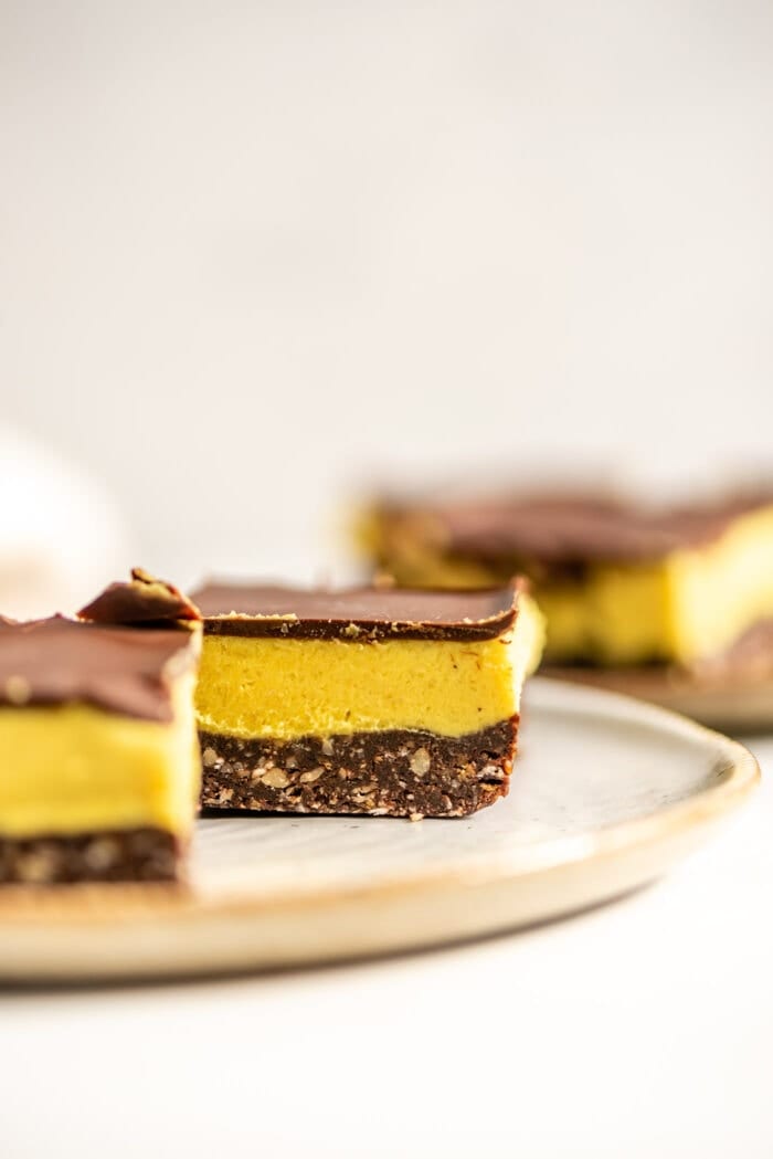 Close up of squares of vegan Nanaimo bar on a small plate. More bars can be seen in the background.