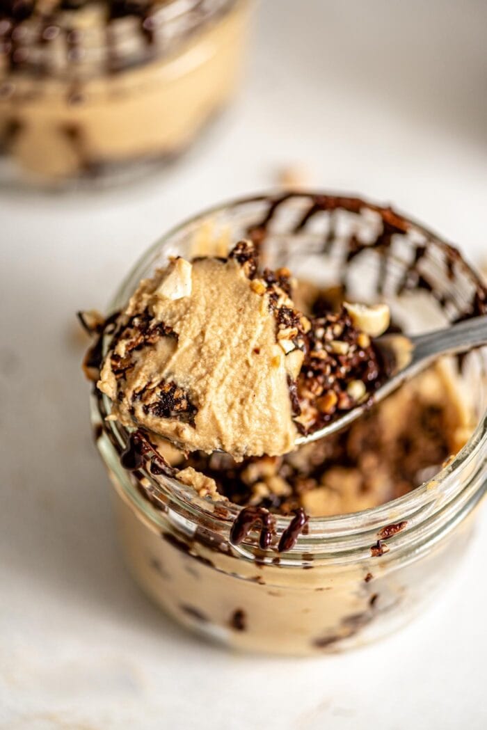 A close up of a spoonful of vegan peanut butter mousse topped with chopped peanuts and chocolate.