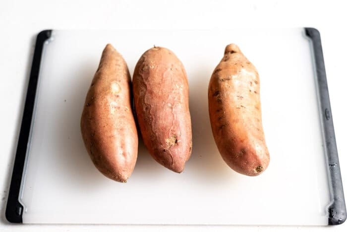 3 whole sweet potatoes on a cutting board.