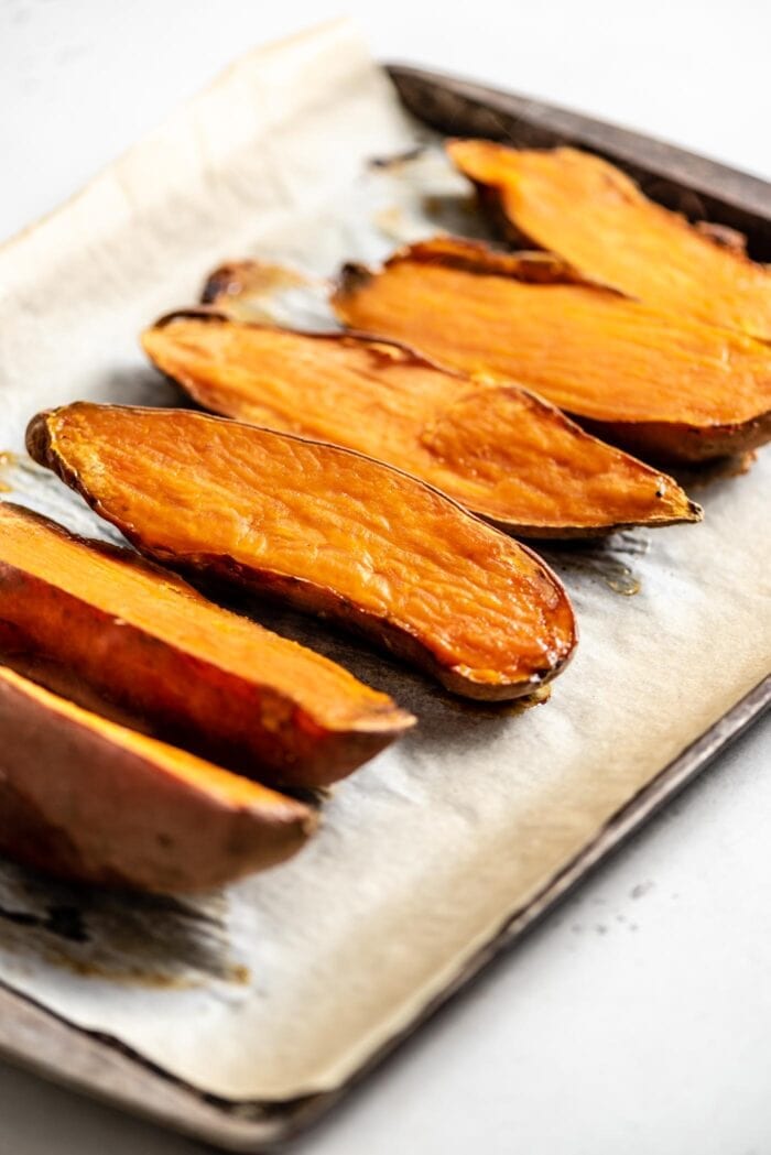 6 baked sweet potato halves on a baking tray lined with parchment paper.
