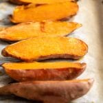 6 baked sweet potato halves on a baking tray lined with parchment paper.