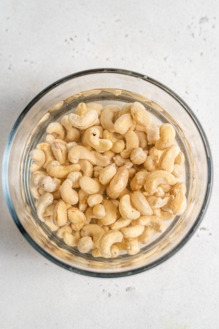 Raw cashews soaking in a glass container.