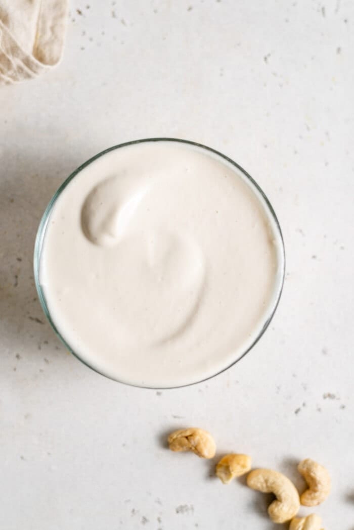 Overhead shot of thick cashew cream in a small glass dish with some raw cashews sitting beside it.