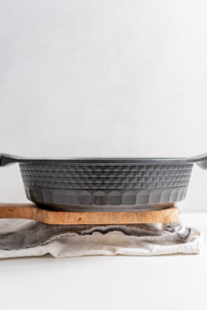 A black frying pan sitting on a block of tofu wrapped in a dish cloth.
