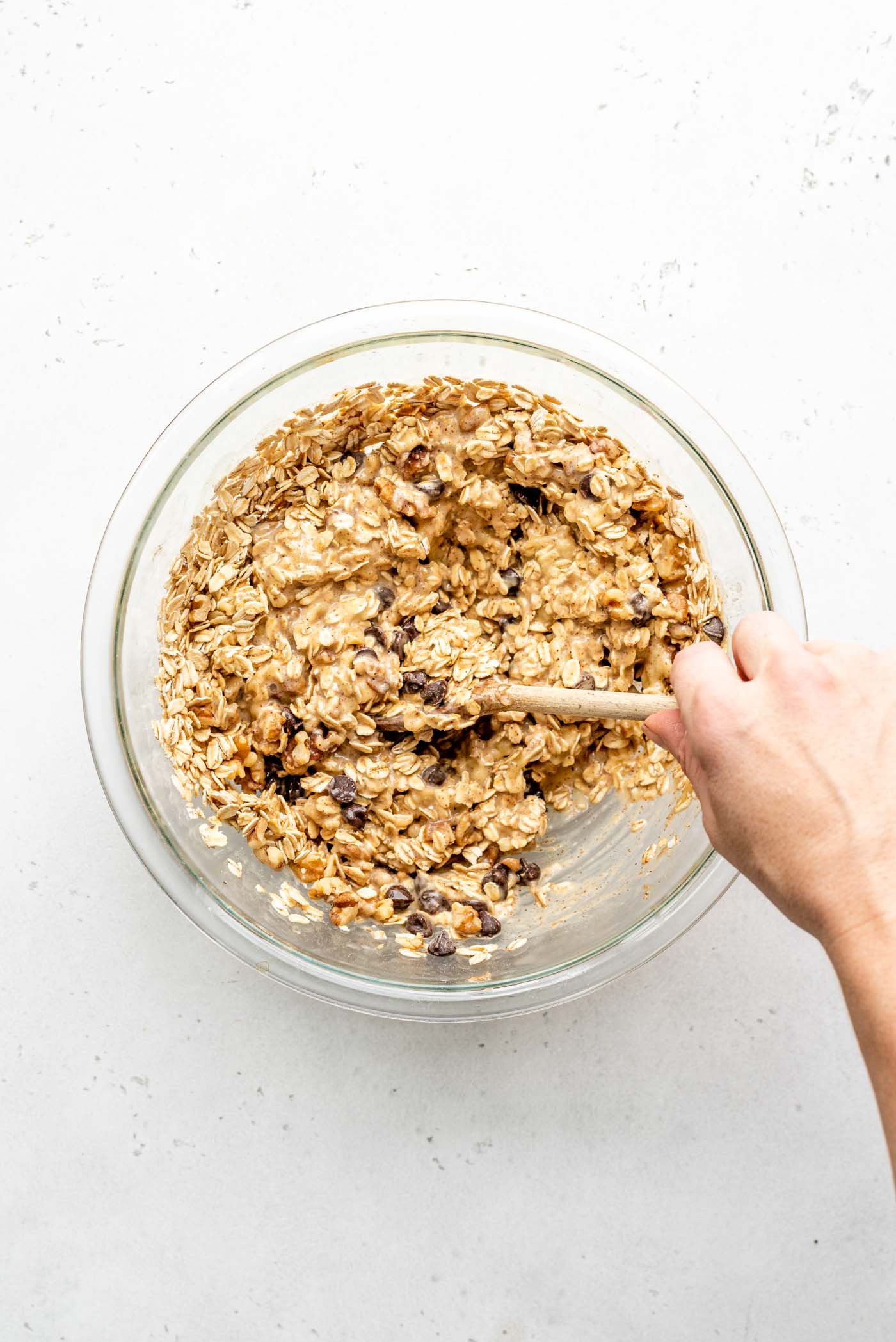 Thick, raw banana oatmeal cup dough in a mixing bowl, showing the combined oats, walnuts, and chocolate chips, ready to be portioned.