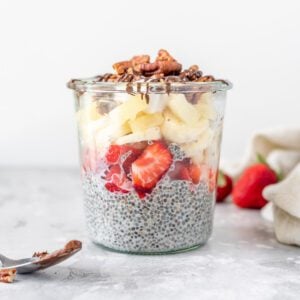 A jar of chia pudding topped with strawberries, banana, pecans and chocolate sauce.