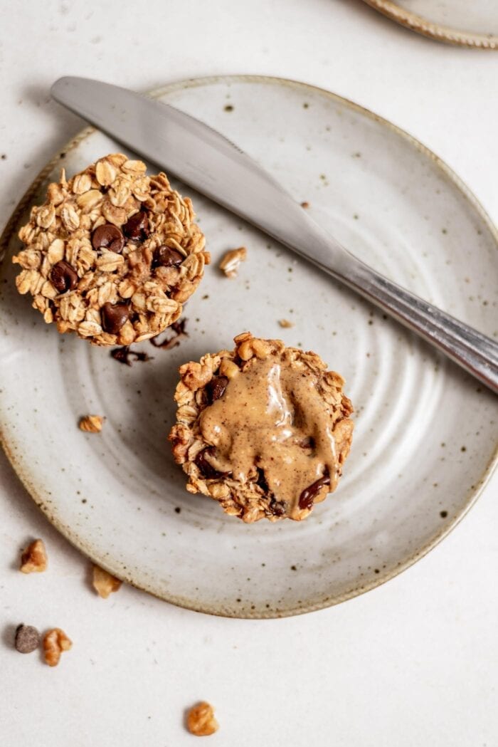 A baked oatmeal cup topped with almond butter sitting on a grey plate with a butter knife.