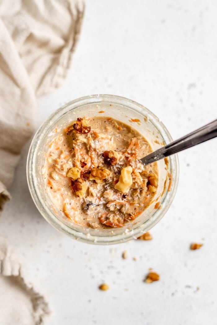 Carrot cake oatmeal with walnuts in top in a glass jar with a spoon.