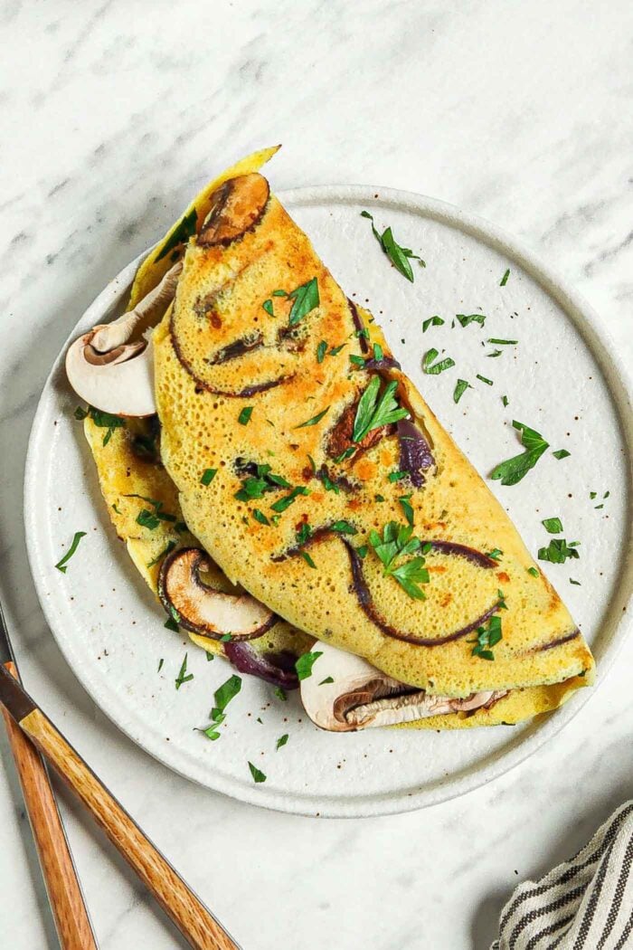 Overhead view of a chickpea flour omelette filled with mushroom and onion on a plate.
