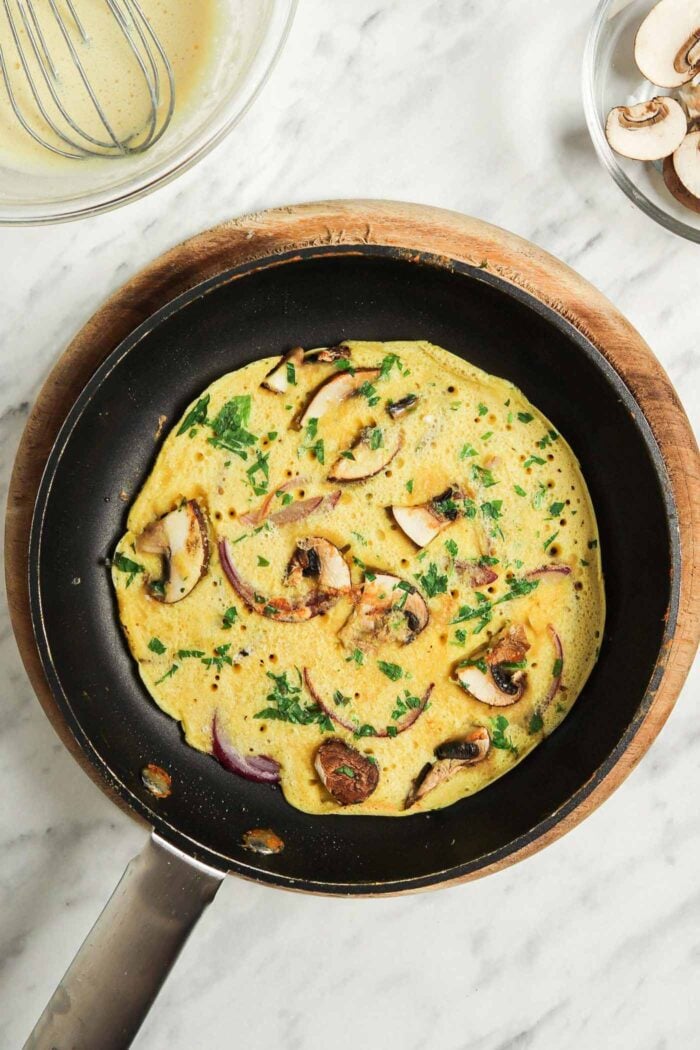 Cooked chickpea omelette with parsley, red onion and mushroom in a small non-stick pan.