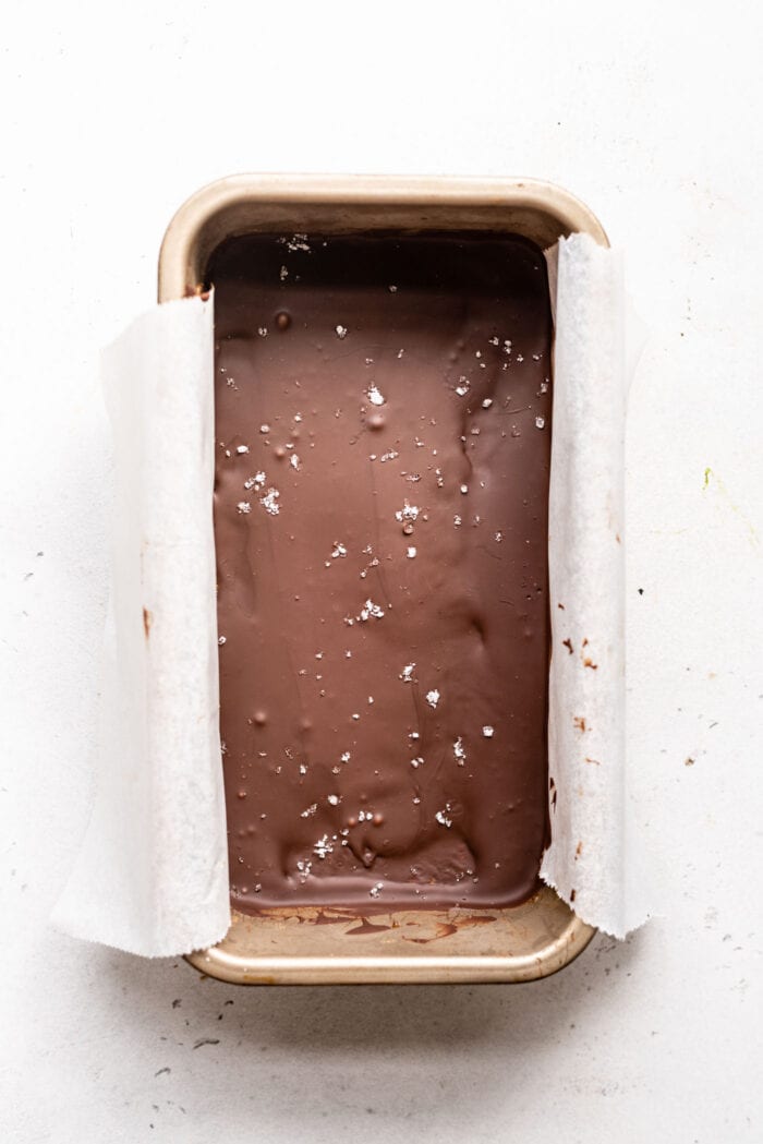 Chocolate caramel bar topped with coarse sea salt in a loaf pan lined with parchment paper.