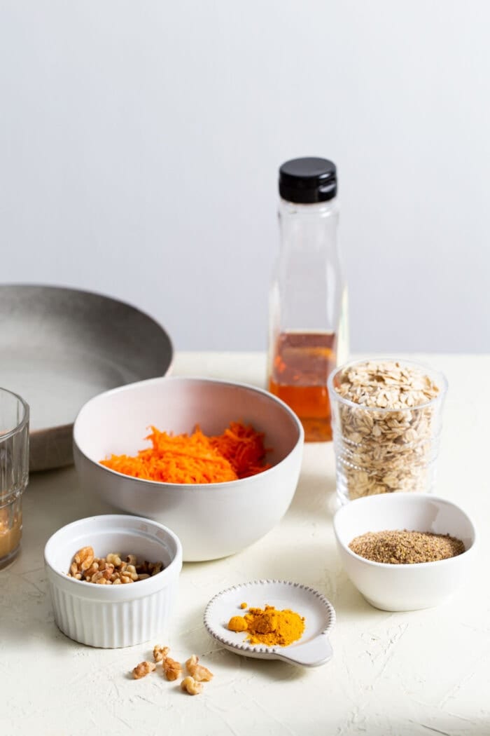 Carrots, walnuts, oats, maple syrup and turmeric in small dishes on a counter top.