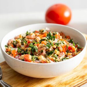 Tabouleh salad in a bowl with a tomato in the background.