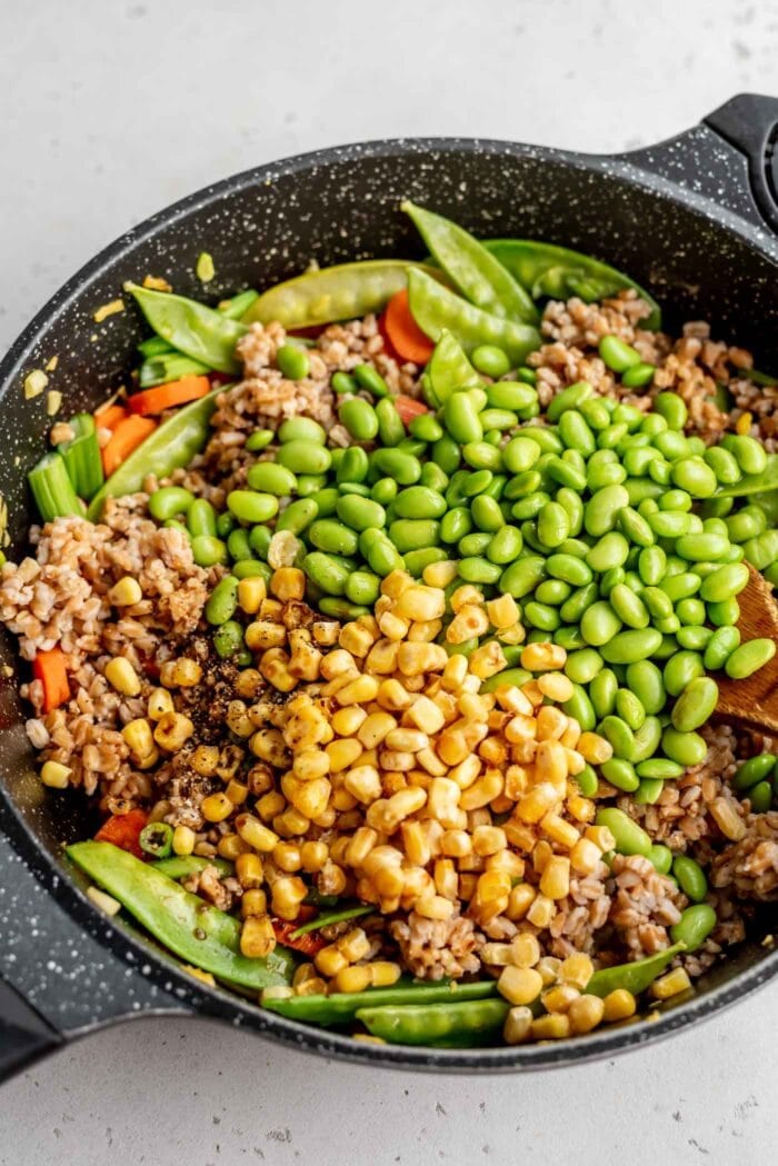 Corn, farro, edamame, carrots and snow peas in a skillet.