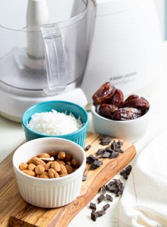 Almonds, coconut, dates and chocolate chips in containers on a countertop.