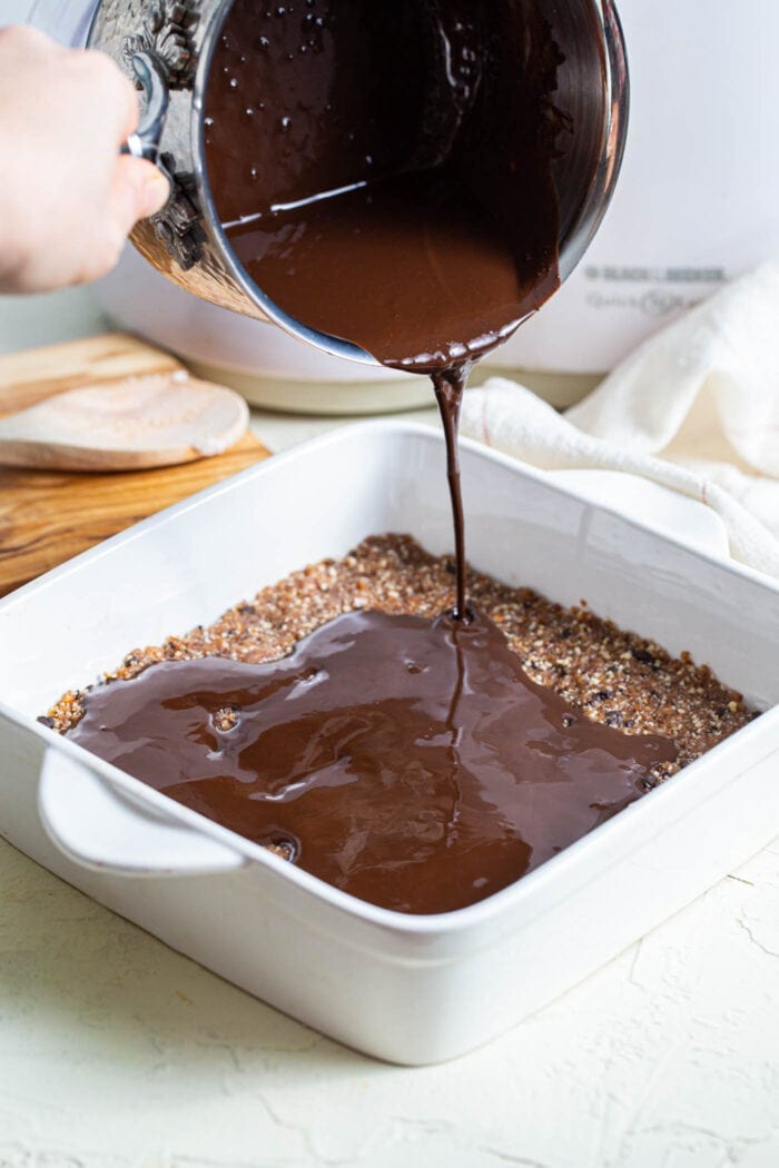 Melted chocolate being poured over bars in a baking pan.