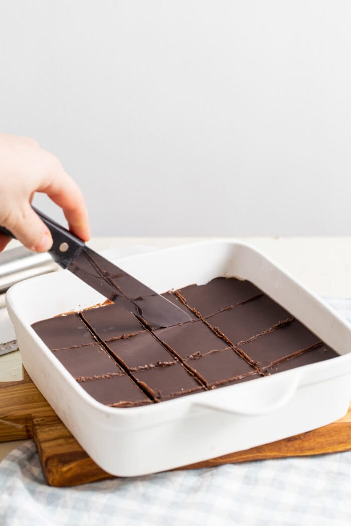 A hand slicing chocolate bars in a pan with a knife.