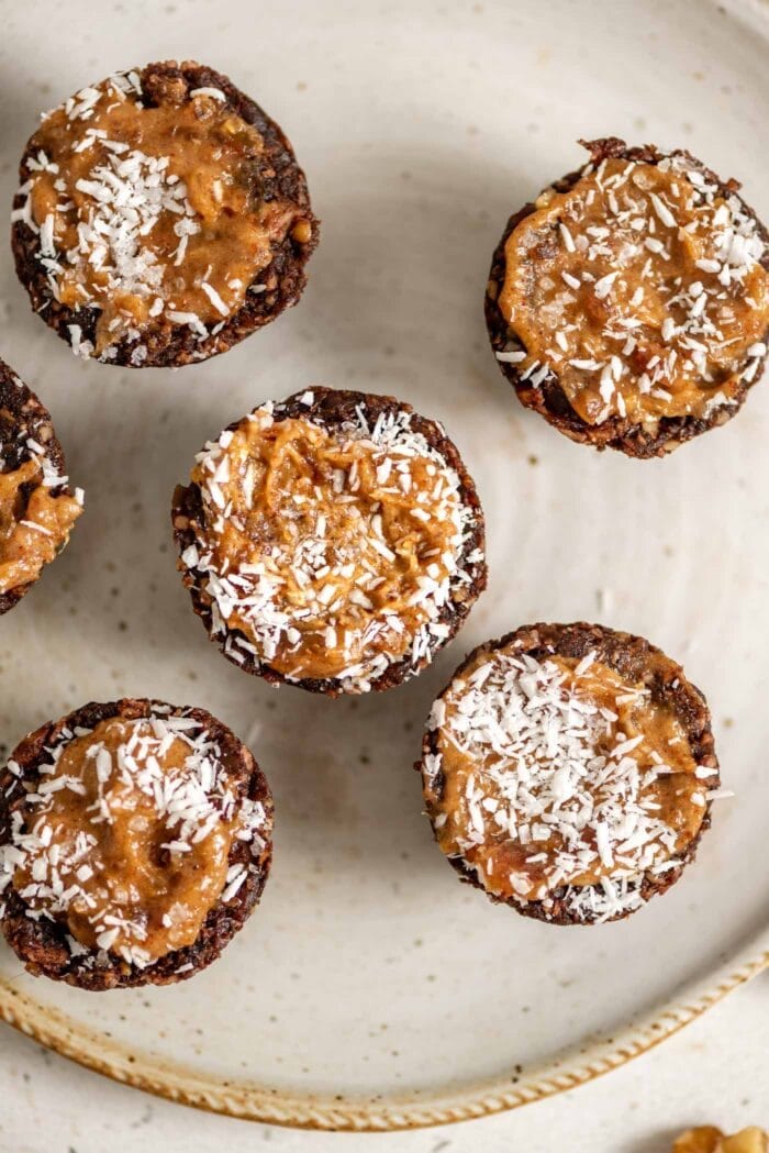 Chocolate tarts with a caramel filling topped with coconut on a small plate.