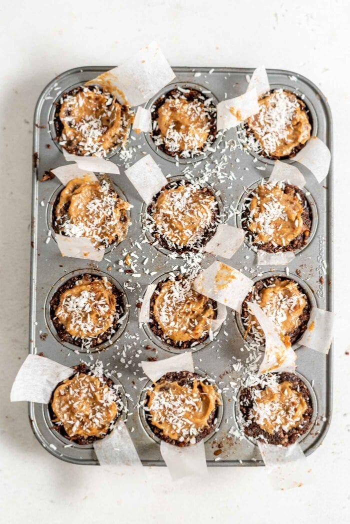 Caramel tarts topped with coconut in a muffin tin.