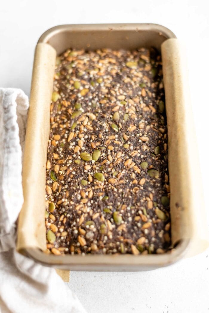 Baked seed bread in a loaf pan with parchment paper.