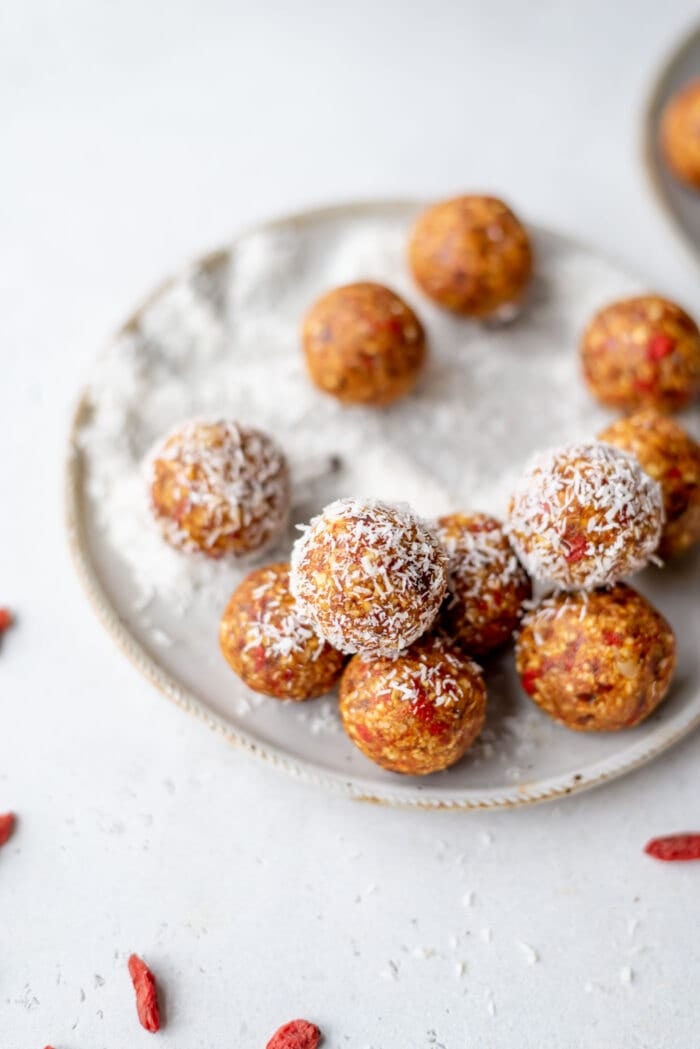 Orange energy balls rolled in coconut on a small plate with some goji berries in the foreground.