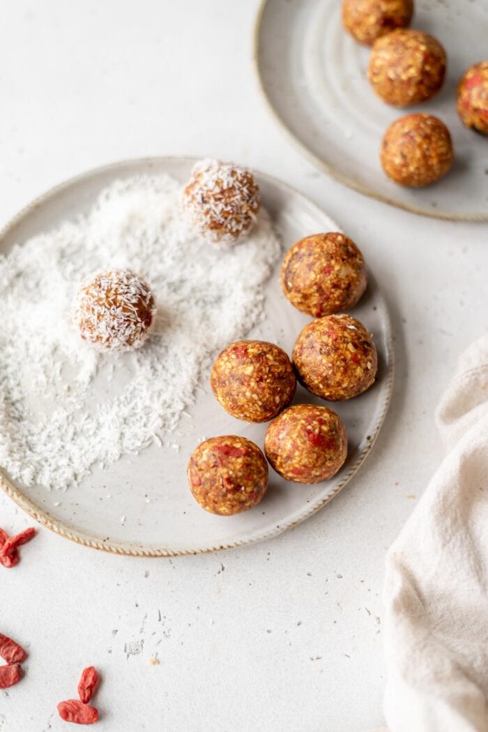 Orange energy balls rolled in coconut on a small plate with some goji berries in the foreground.