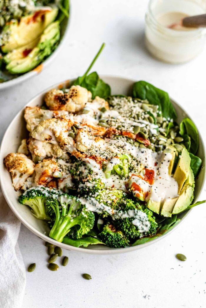 Avocado, roasted cauliflower, broccoli, spinach and seeds topped with tahini dressing in a bowl.