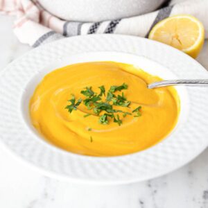 Bowl of creamy cashew carrot soup with a spoon in it.