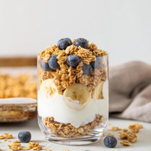 Yogurt, sliced banana and granola parfait in a glass topped with blueberries.