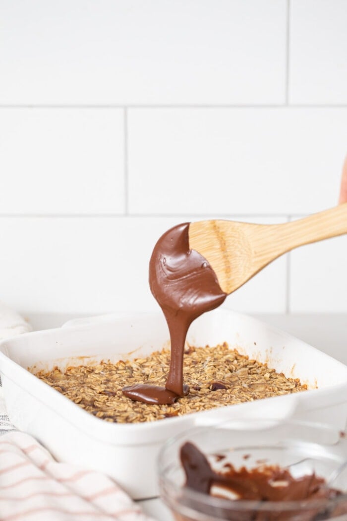 Spooning melted chocolate over baked oatmeal bars.